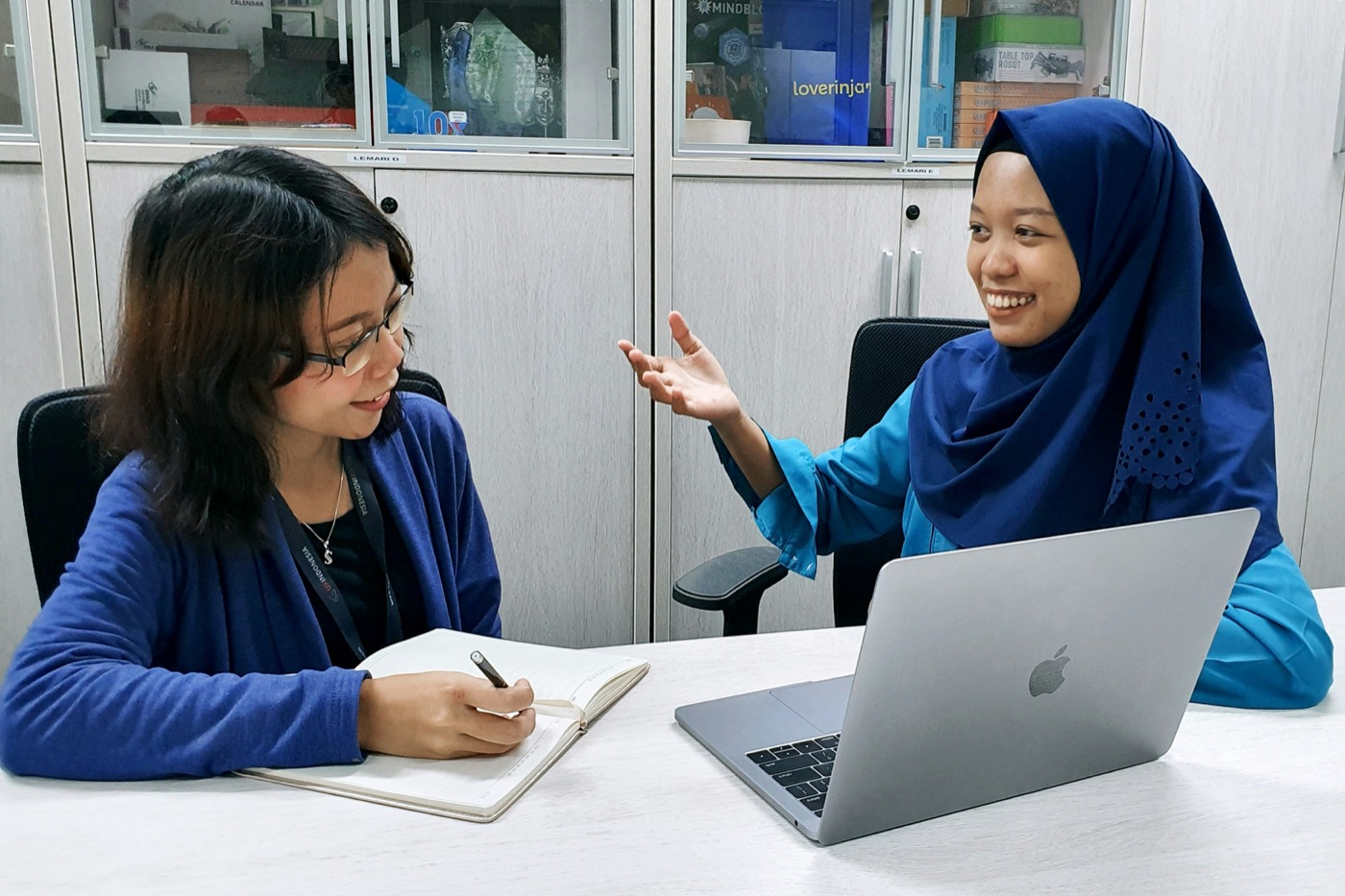 Two colleagues comparing notes beside an open notebook and laptop