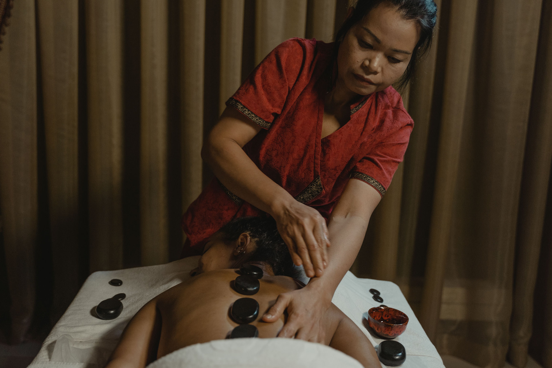A local therapist delivering a hot-stone massage in a spa treatment room