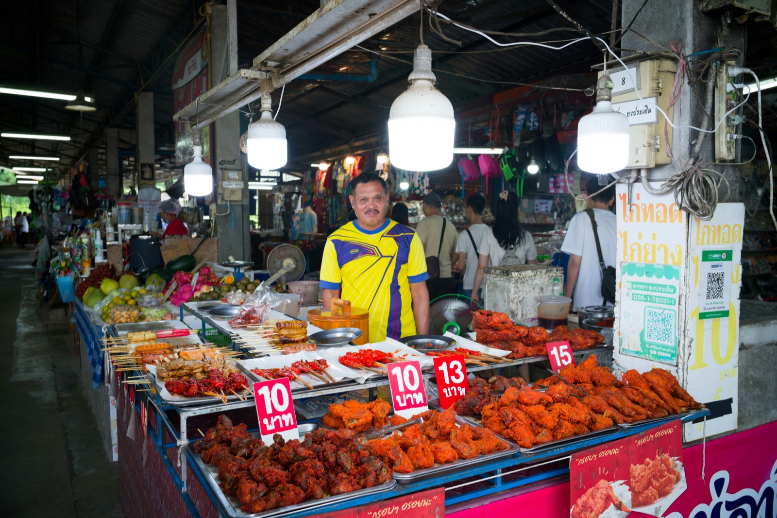 Stallholder standing behind priced skewers and fried chicken at a covered market